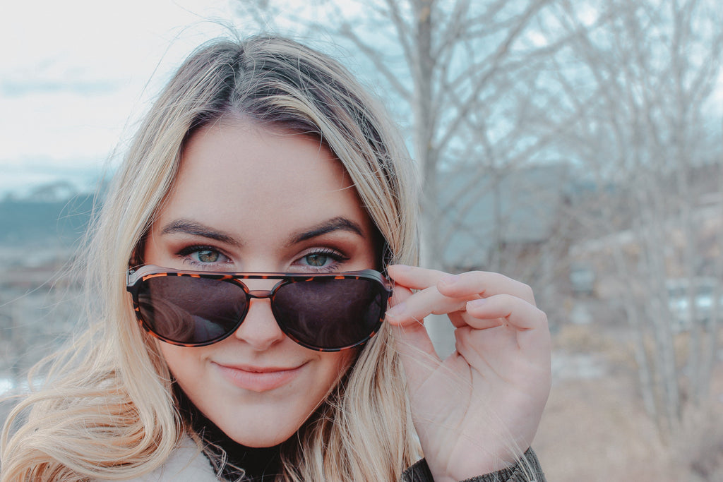 Woman wearing Optic Nerve Govnah sunglasses with a tortoise frame and smoke lenses with a natural background