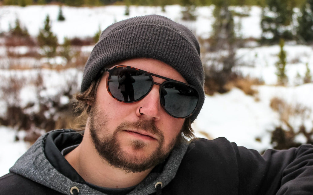 Man wearing a brown beanie and Optic Nerve Govnah sunglasses with a tortoise frame and smoke lenses with a natural snowy background