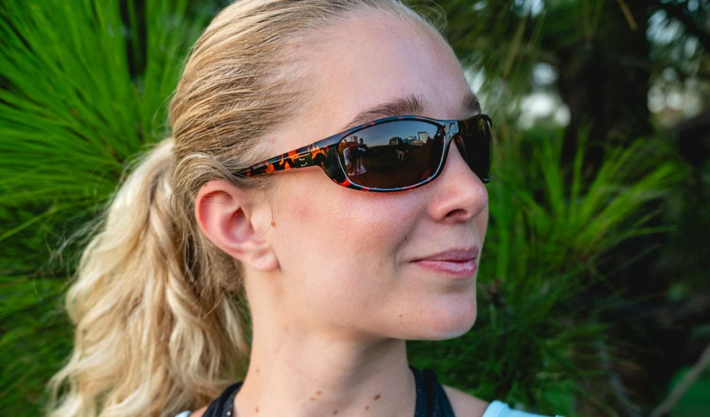Close up of a woman wearing Optic Nerve Backwoods sunglasses with a tortoise frame and brown lenses with a natural background