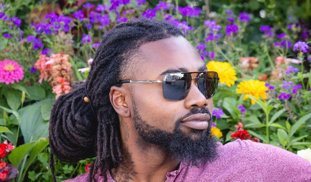 Close up of a man wearing Optic Nerve Dragoon sunglasses with a gunmetal frame, smoke lenses, and a silver mirror, with a natural flower background