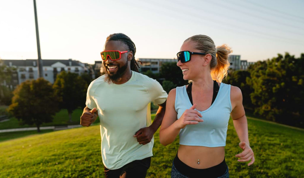 Two people running up a hill wearing Optic Nerve FixiePHENOM sunglasses with buildings in the background