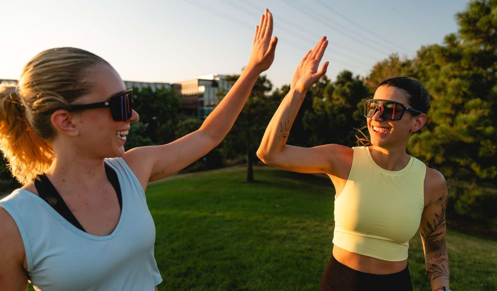 Two people high fiving wearing Optic Nerve FixiePHENOM sunglasses with a natural background