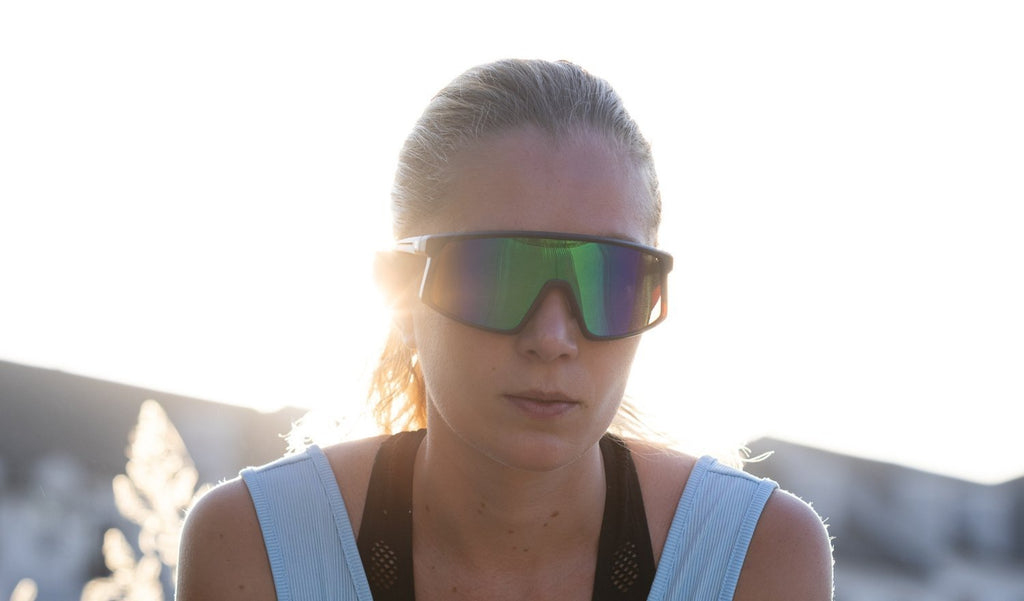 Close up of a woman wearing Optic Nerve Stone Cat sunglasses with a tortoise frame, brown lens, and a green mirror with the sun shinning behind her head