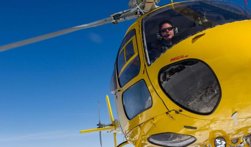 Man piloting a yellow helicopter wearing Optic Nerve sunglasses