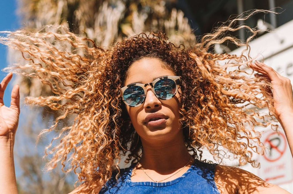 Woman wearing Optic Nerve Rizzo sunglasses with a tortoise frame, smoke lenses, and a blue mirror with a blurred background.